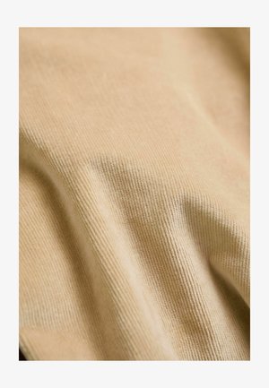 Beiger Stoff mit einer gerippten Textur, der weiche, leicht glänzende Fasern zeigt. Das Layout ist drapiert und betont den Fluss und die Konturen des Materials.