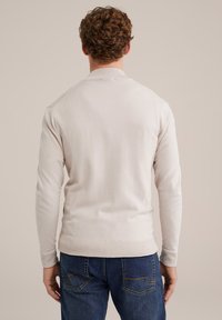 Helles beiges Strickpullover mit langen Ärmeln und geripptem Saum, kombiniert mit blauen Jeans. Der Pullover hat ein nahtloses Rückendesign.