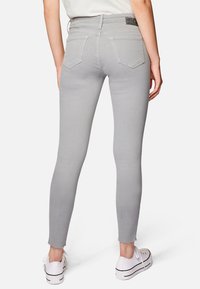 Jeans skinny grigi con orlo sfrangiato, design a cinque tasche, vita a media altezza e cuciture sottili. Abbinati a sneakers bianche.