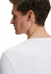 T-shirt bianco a manica corta con scollatura ampia, mostrato su una persona di spalle. Il materiale appare morbido e liscio, design minimale.