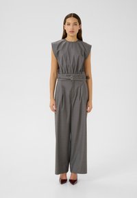 Completo grigio su misura composto da un top senza maniche con vita arricciata e pantaloni a gamba larga, completato da una cintura coordinata e scarpe a punta.