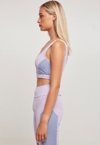 En lys lilla sportbh med lyseblå detaljer og høy midje matchende tights, med en tettsittende design og glatt tekstur.