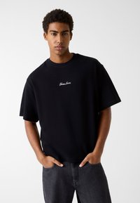 Czarny t-shirt z krótkim rękawem i okrągłym dekoltem, z haftowanym białym logo "Gaps Jeans" na piersi, wykonany z bawełnianej tkaniny.