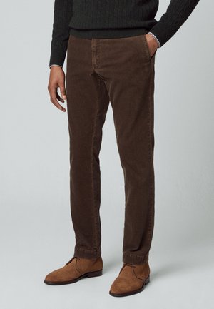 Bruine corduroybroek met een rechte pasvorm, voorzien van voorzakken en een subtiele textuur, gedragen met tan kleurige suède laarzen.