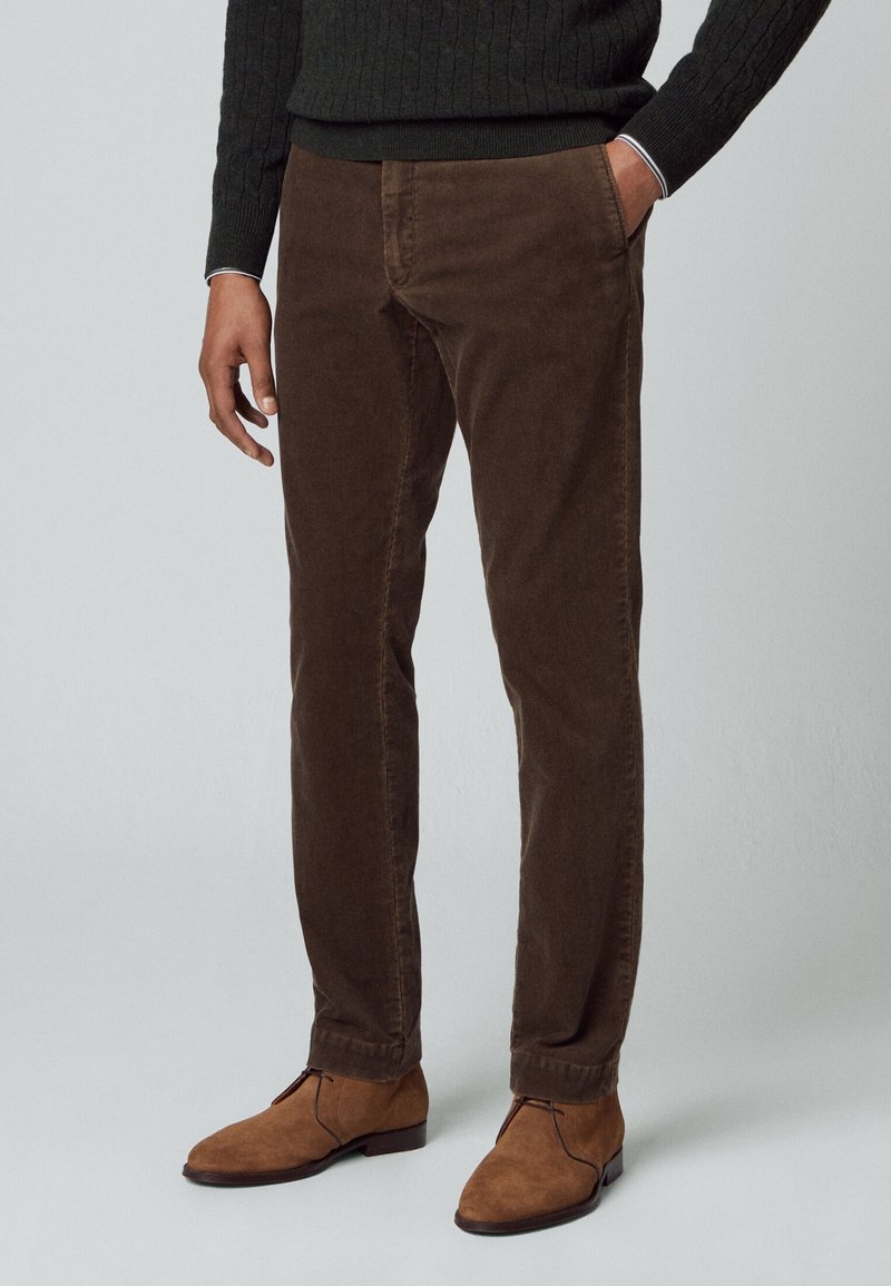 Pantalones de pana marrones con corte recto, que cuentan con bolsillos frontales y una textura sutil, usados con botas de ante color marrón claro.