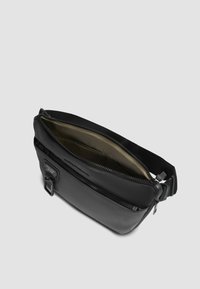 Zwarte leren crossbodytas met een ritssluiting, voorzien van een gladde textuur, verstelbare band en een voering aan de binnenkant in olijfgroen.