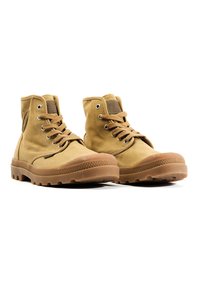 Bottines en toile beige avec semelle en caoutchouc marron, bout rond, design à lacets et rembourrage sur les côtés. Présente des motifs texturés et des œillets.