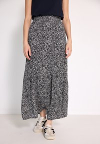 Schwarzer und weißer gemusterter Maxirock mit hoher Taille, schwingendem Design und weichem Stoff, kombiniert mit beigen Sneakers mit schwarzen Akzenten.