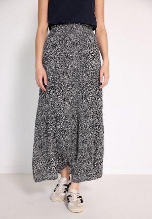 Gonna maxi bianca e nera a fantasia con vita alta, design svasato e tessuto morbido, abbinata a sneaker beige con dettagli neri.