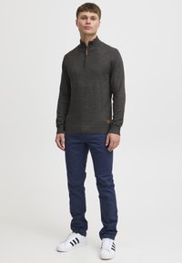 Dark gray sweater with high collar and front zipper, worn with navy blue pants and white sneakers featuring black stripes. Brown logo patch visible.