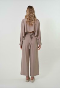 Ensemble chic en deux pièces de couleur taupe clair. Le top court présente un dos ouvert et des manches longues, tandis que le pantalon à jambes larges dispose d'une taille à nouer. Texture lisse.