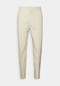 Béžové bavlněné kalhoty s elastickým pasem, zúženým střihem nohou a dvěma předními kapsami. Hladký povrch bez výrazných vzorů.