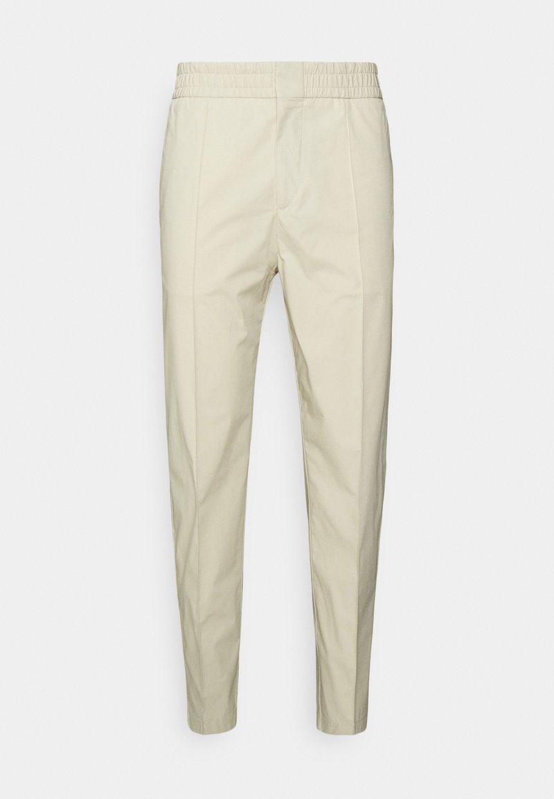 Béžové bavlněné kalhoty s elastickým pasem, zúženým střihem nohou a dvěma předními kapsami. Hladký povrch bez výrazných vzorů.