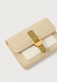 Portofel din piele texturată bej, cu buzunar frontal alb și curea verde măslin fixată cu un clips auriu, pe fundal alb.