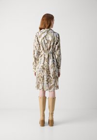 Rochie tip wrap din material ușor, cu un imprimeu floral de frunze verzi și albastre, are mâneci lungi și talie strânsă. Este asortată cu cizme bej până la genunchi.