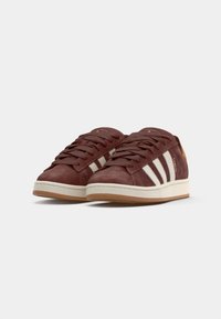Brune suede sneakers med hvide striber, snørebåndsdesign, polstret gummisål og en tan accent ved hælen.