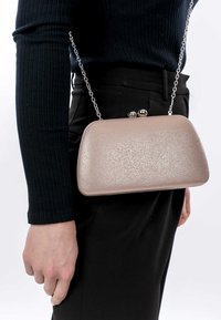 Borsa a pochette in materiale testurizzato rosa chiaro con tracolla in catena argentata, forma arrotondata e due dettagli metallici con gancio nella parte superiore.
