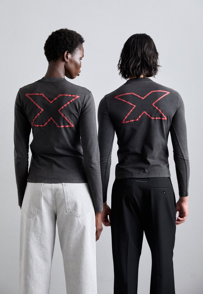 Graue Langarmshirts mit großen roten "X"-Designs auf dem Rücken, getragen mit weißen und schwarzen Hosen. Schlichte und moderne Schnittführung.