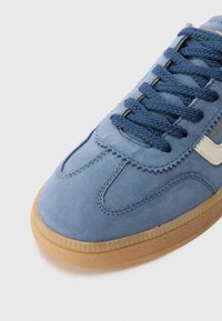 Sinine nubukist sneaker, millel on tekstuuriga pind, ümar varvas, valge külgaksent ja sinised paelad. Omab kummist välistalla.