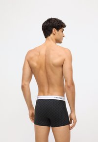 Melnas bokseršortas ar ģeometrisku rakstu, balta jostas daļa ar zīmolu "Calvin Klein". Mīksta auduma un pieguļoša dizaina.