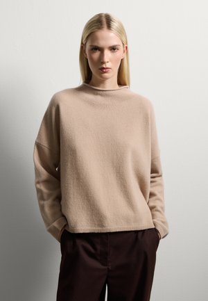 Maglioncino beige a maglia con collo alto, vestibilità ampia e maniche lunghe, abbinato a pantaloni a sigaretta marrone scuro. Tessuto morbido, design minimale.