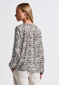 Blusa a maniche lunghe in tessuto leggero con motivo astratto bianco e nero, dal taglio morbido e dettagli arricciati sul retro.