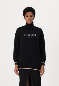 Zwarte coltrui met "LIU JO 1995" in steentjes, met beige gestreepte accenten bij de boorden en de zoom, en een ontspannen pasvorm.