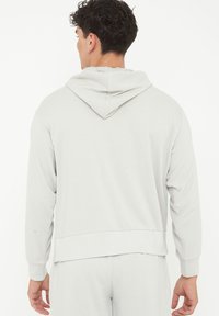 Ljusgrå munkjacka med en avslappnad passform. Har långa ärmar, ribbade ärmslut och en kenguruficka. Mjuk och slät textur.