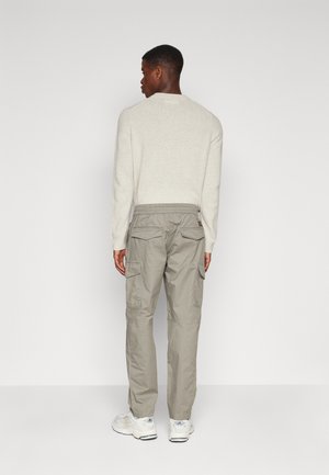 Pantalons cargo gris clair avec plusieurs poches, taille élastique et coupe décontractée, associés à un pull de couleur crème.