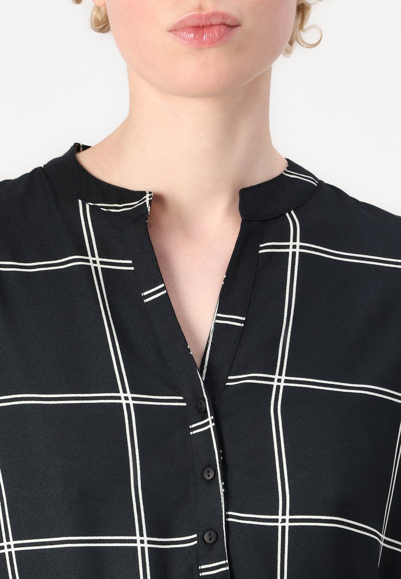 Schwarzes Hemd mit Kragen, das mit einem weißen Karomuster versehen ist, Knopfverschluss und einer weichen Stofftextur aufweist. Der Halsausschnitt ermöglicht ein einfaches Tragen.