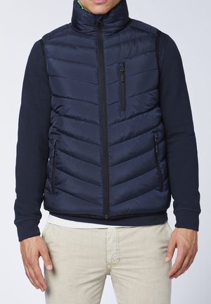 Navy puffer vest with quilted pattern, high collar, and black zippers. Lightweight material, combined with a solid navy long-sleeve shirt underneath.