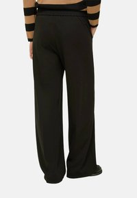 Pantaloni neri a gamba larga con una texture liscia e vita elasticizzata, caratterizzati da tasche laterali discrete e una vestibilità comoda.