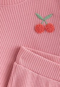 Lyserød ribbet sweater med broderet kirsebærdesign med orange pom-pom kirsebær og grønne blade. Blødt, tekstureret stof.