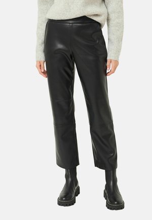 Person iført sorte lædercropped bukser parret med sorte chunky ankelstøvler og en lysegrå strikket sweater.