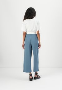 Witte top met korte mouwen en een gedraaide achterkant, gecombineerd met hoogstaande lichtblauwe wijde broek en zwart chunky-heeled sandalen.