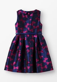 Abito senza maniche di un blu scuro con motivi a fiocchi fucsia. Presenta un colletto, chiusura con bottone sul retro e un design di gonna svasata.