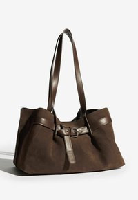 Pruun sametist õlakott, millel on sileda pruuni nahaga aktsendid ja vööstile sarnane sulgemine. Omab kahe pikka rihma, et kanda seda mugavalt.