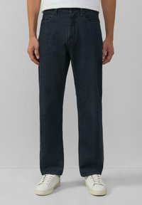 Donkerblauwe spijkerbroek met een rechte pasvorm, vijf zakken en een klassieke stijl, gecombineerd met witte sneakers op een neutrale achtergrond.