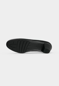 Semelle noire d'une chaussure de ville pour femme avec une semelle texturée et un petit talon carré sur un fond clair uni.