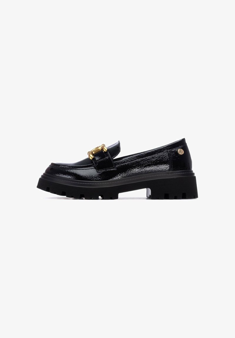Mocasín de charol negro con una suela gruesa y texturizada. Presenta una hebilla decorativa dorada en la correa y un diseño de punta redondeada.