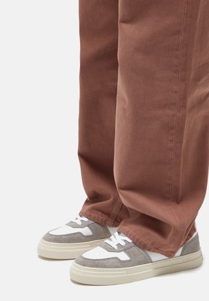 Sneaker grigie e bianche con una tomaia testurizzata, dotate di una suola liscia e un design con lacci, indossate con pantaloni marroni larghi.