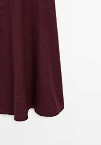 Burgundininen pellavahame, jossa on virtaava muotoilu, leikattu puoliväliin pohkeita, joka on pehmeä tekstiili ja siinä on hienostunutta ommelta helmassa.