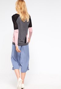 Grå och rosa långärmad topp med svarta nätinslag; kombinerad med lösa blå culotter och vita sneakers. Mjuk tygtextur.