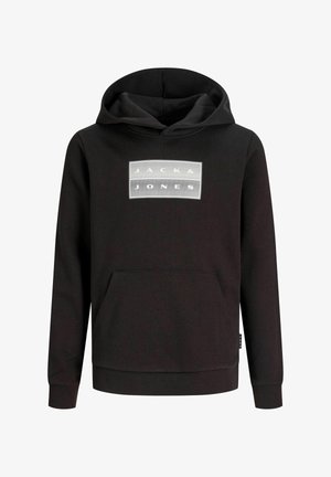 Garçon portant un sweat à capuche noir, un pantalon vert olive, des baskets noires et une casquette de baseball noire, debout et regardant sur le côté sur fond blanc.