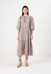 Mauve midi-klänning med puffärmar, knytdetalj vid halsen och lager-skirt. Matchad med beige sandaler med remmar. Slät, lättviktig tyg.