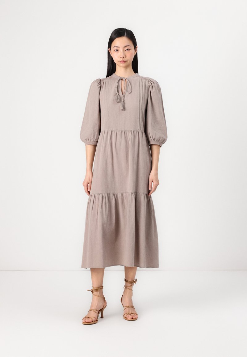 Mauve midi-klänning med puffärmar, knytdetalj vid halsen och lager-skirt. Matchad med beige sandaler med remmar. Slät, lättviktig tyg.