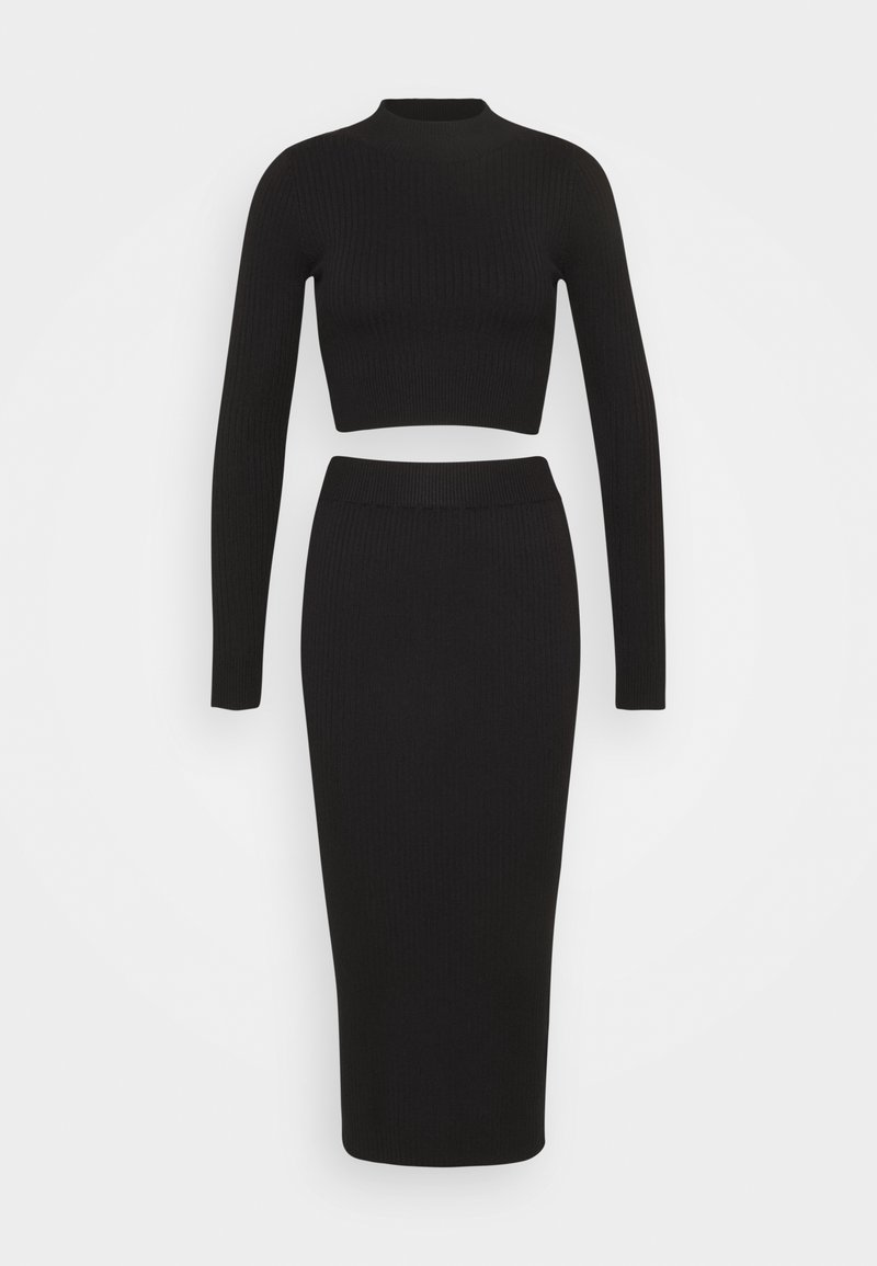 Ensemble deux pièces en maille côtelée noire avec crop top à manches longues et jupe midi taille haute et ajustée sur fond uni.