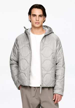 Light gray puffer jacket with a quilted design and a hood, featuring front zipper pockets and a streamlined fit. Worn over a white shirt.
