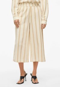 Krēma krāsas bikses ar platu kāju un vertikāl�ām dzeltenām un brūnām svītrām, elastīga jostasvieta un viegls audums. Apvienotas ar melniem augstpapēžu sandales.