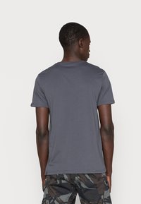 Tricou gri cu mânecă scurtă, fabricat dintr-un material moale, având un guler clasic și o croială lejeră. Vederea din spate nu prezintă grafice sau modele.